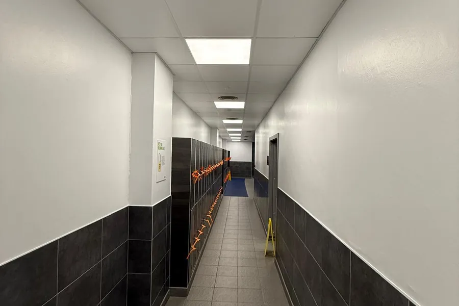 Long corridor with painted walls, dark tiled dado and suspended ceiling