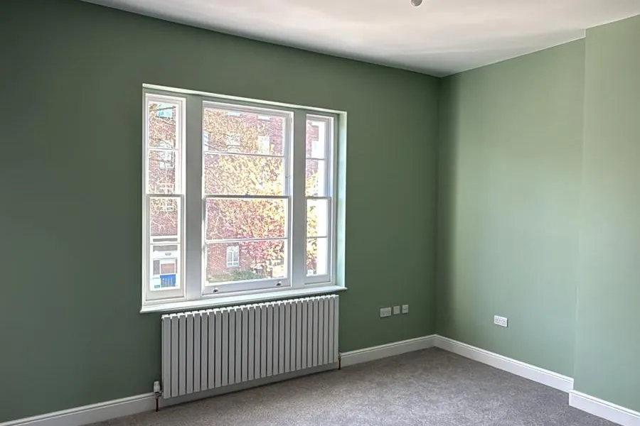 Bedroom decorated in sage green with white woodwork and a sash window